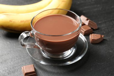 Cam bardakta lezzetli çikolatalı süt, siyah masada parçalar ve muzlar, yakın plan.