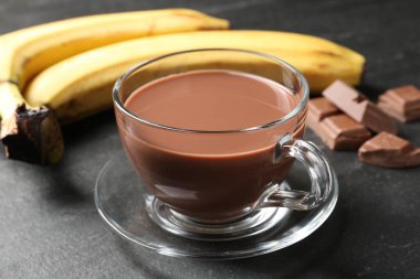 Cam bardakta lezzetli çikolatalı süt, siyah masada parçalar ve muzlar, yakın plan.