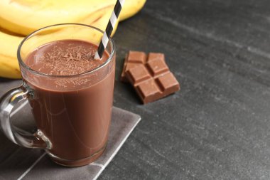 Cam bardakta lezzetli çikolatalı süt, siyah masada parçalar ve muzlar, yakın plan. Metin için boşluk