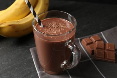 Cam bardakta lezzetli çikolatalı süt, siyah masada parçalar ve muzlar, yakın plan.