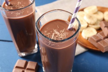 Lezzetli çikolatalı süt bardaklarda, parçalar ve muz mavi ahşap masada, yakın plan