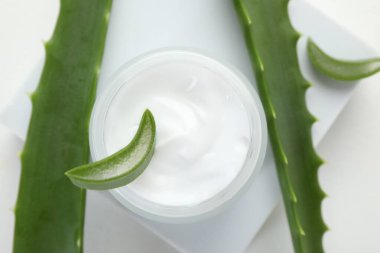 Aloe vera özütüyle nemlendirici krem ve beyaz arkaplanda yapraklar, düz bir zemin.