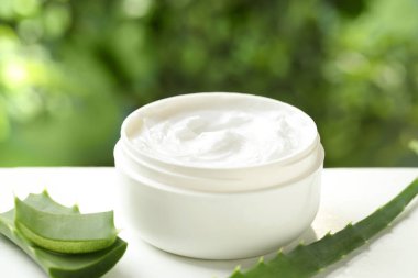 Kavanozda aloe vera özütüyle nemlendirici krem ve beyaz ahşap masa üzerindeki yaprakları bulanık yeşil arka planda, yakın plan