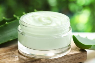 Kavanozda aloe vera özütüyle nemlendirici krem ve bulanık yeşil arka plana karşı beyaz masadaki yaprakları kesme, yakın plan