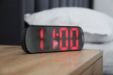 Dijital alarm saat 11 'de kapalı bir odada, komodinin yanında.