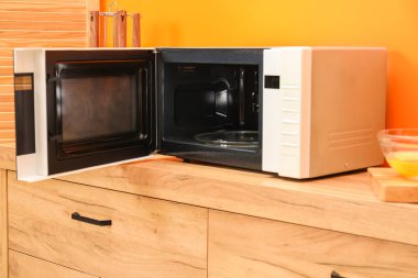 Turuncu duvarın yanındaki ahşap dolapta mikrodalga fırını aç.