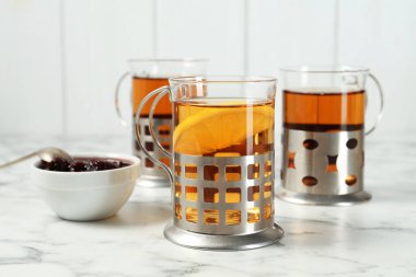Glasses of tea in metal holders served on white marble table, closeup