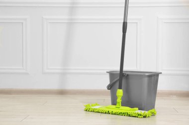 Beyaz duvarın yanındaki tahta zeminde mikrofiber paspas ve kova. Metin için boşluk