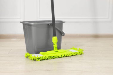 Beyaz duvarın yanındaki tahta zeminde mikrofiber süpürge ve kova.