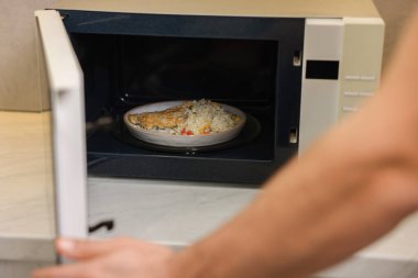 Yemek tabağını mikrodalgaya koyan adam, yakın plan.