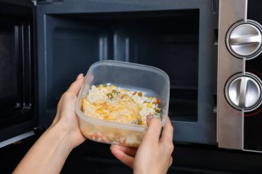 Kadın yemeğiyle birlikte mikrodalgaya konteynır koyuyor. Kapalı mekanda.