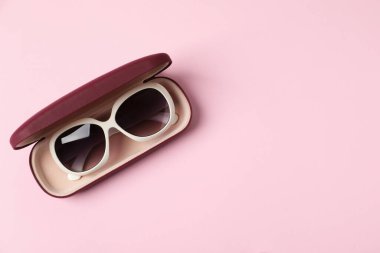 Açık pembe arka planda şık güneş gözlüklü bir çanta, üst manzara. Metin için boşluk