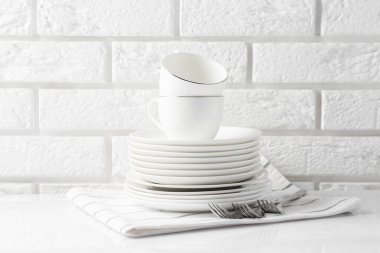 Different clean dishware on white table near brick wall