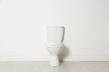 Beyaz duvarın yanındaki seramik klozet.