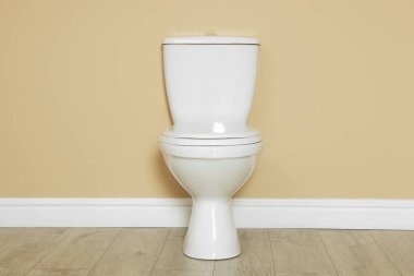 Bej duvarın yanındaki seramik klozet.