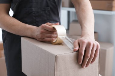 Kapalı alanda yapıştırıcı bantlı karton kutu mühürleyen adam.