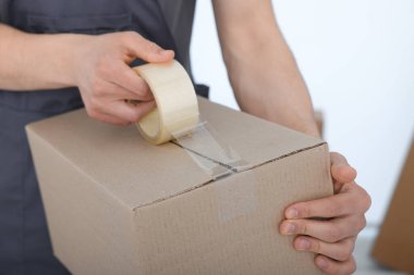 Kapalı alanda yapıştırıcı bantlı karton kutu mühürleyen adam.