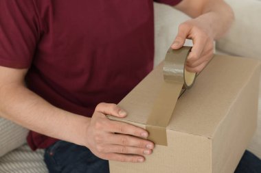 Kapalı alanda yapıştırıcı bantlı karton kutu mühürleyen adam.