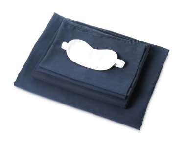 Beyaz arka planda ipeksi çarşaf ve uyku maskesi yığını.