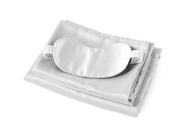 Beyaz arka planda ipeksi çarşaf ve uyku maskesi yığını