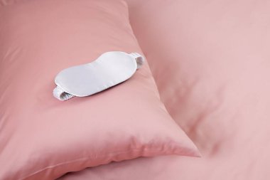 Güzel pembe ipek çarşaflar ve uyku maskesi olan bir yatak, yakın plan. Metin için boşluk