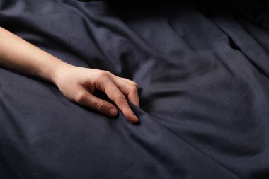 Yatakta koyu mavi ipek çarşaflara dokunan kadın, yakın plan.