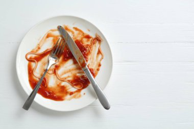 Kirli tabak ve çatal bıçak takımı beyaz ahşap masada, üst manzara. Metin için boşluk