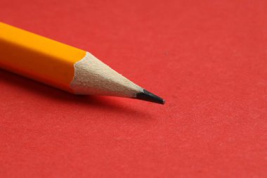 Kırmızı arka planda keskin bir grafit kalem, yakın plan. Metin için boşluk