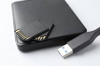 Beyaz arkaplanda USB kablosu ve SD hafıza kartı olan harici sabit disk, kapat