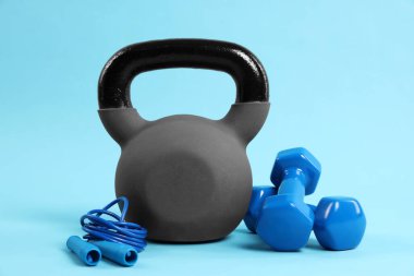 Kettlebell, atlama ipi ve açık mavi arkaplanda dambıllar.