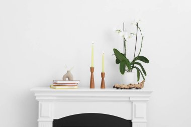 Beyaz duvarın yanındaki şöminede yanan mumlar ve diğer dekorlarla süslü şamdanlar.