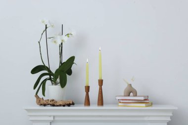 Beyaz duvarın yanındaki şöminede yanan mumlar ve diğer dekorlarla süslü şamdanlar.