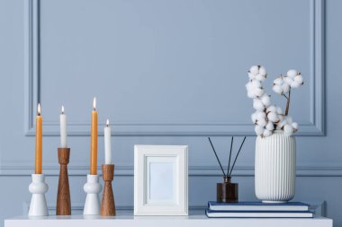 Yanan mumlarla süslü şamdanlar vazoda pamuk çiçekler ve gri duvarın yanındaki beyaz masada diğer dekorlar.
