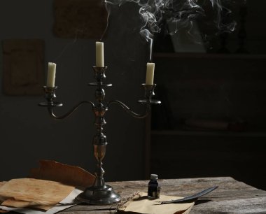 Şamdandaki mumlar, eski kağıtlar, mürekkep hokkası ve tüy kapalı masa üzerinde.