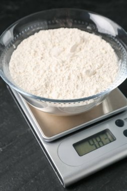 Elektronik mutfak terazisi ve koyu dokulu bir kase un, yakın plan.