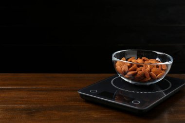 Elektronik mutfak terazisi ve siyah arka planda bir kase badem fıstığı. Metin için boşluk