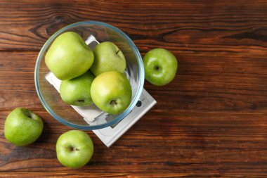 Elektronik mutfak terazisi ve ahşap masada bir kase yeşil elma. Metin için boşluk