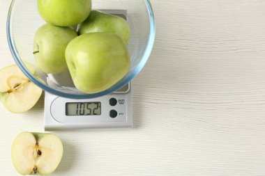 Electronic kitchen scale with bowl of green apples on white wooden table, flat lay. Space for text