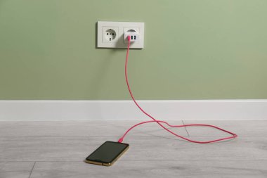 Kablolu USB adaptörü elektrik prizine takılı, akıllı telefonu içeride şarj ediyor.