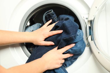 Kadın çamaşır makinesine kot pantolon koyuyor, yakın plan.