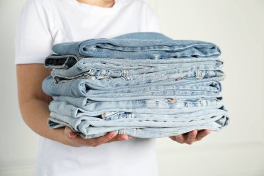 Kapalı alandaki aydınlık duvarın yanında farklı şık kot pantolonları olan kadın, yakın plan.