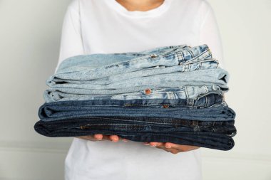 Kapalı alandaki aydınlık duvarın yanında farklı şık kot pantolonları olan kadın, yakın plan.