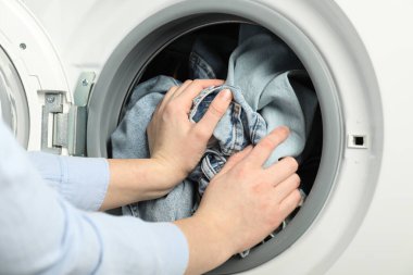 Kadın çamaşır makinesine kot pantolon koyuyor, yakın plan.