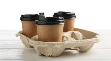 Kağıt kahve bardakları beyaz ahşap masadaki karton tutacakta, yakın plan.