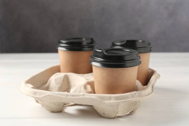 Kağıt kahve bardakları beyaz ahşap masadaki karton tutacakta, yakın plan.