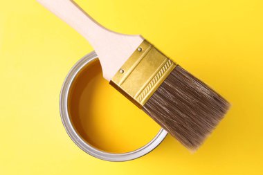 Can of bright paint and brush on yellow background, top view