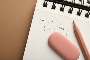 Kahverengi arkaplanda silgi, kalem, kırıntı ve defter, üst görünüm