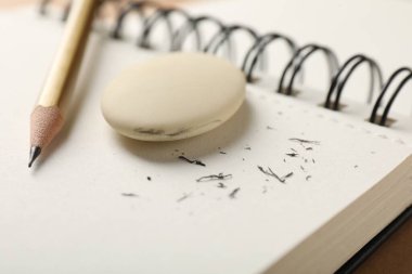 Eraser, pencil, scraps and notebook on brown background, closeup