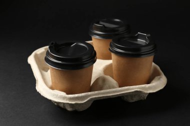 Kağıt kahve bardakları siyah arka planda karton tutucu, yakın plan.