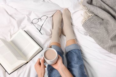 Bir fincan sıcak içecekle yatakta bej çorap giyen bir kadın.